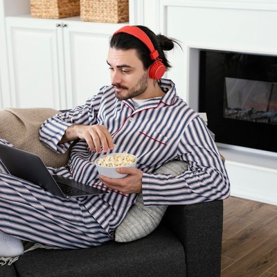 homem de pijamas longos sentado no sofá comendo pipoca