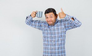homem de pijama segurando caneca com uma mao e fazendo sinal positivo com a outra mao