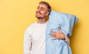 homem em fundo amarelo com pijama masculino flanelado segurando travesseiro