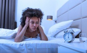 mulher na cama olhando para o relógio por não ter qualidade do sono